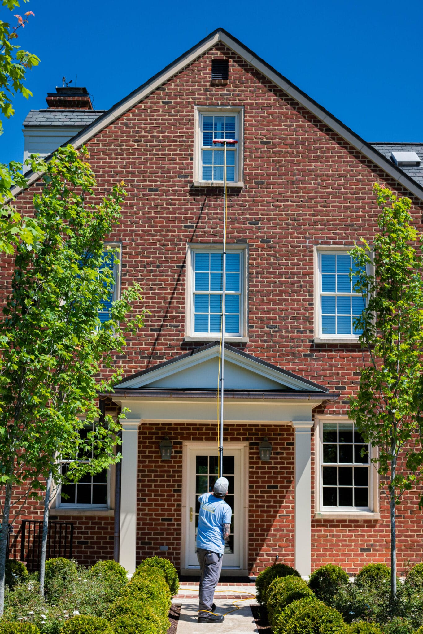 Professional window cleaner using tools to clean large commercial building windows on a sunny day.